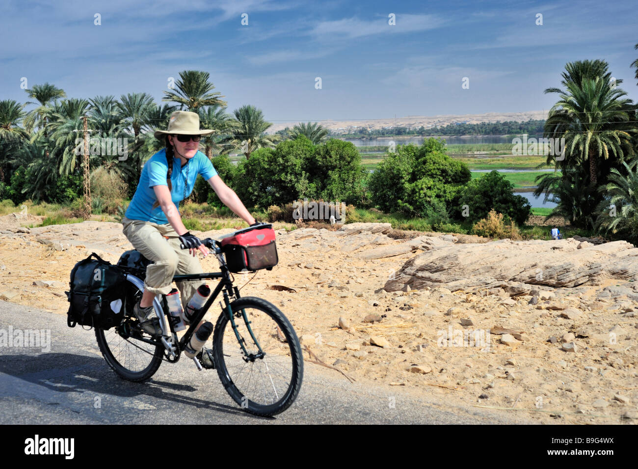 Jeune femme western touring cyclist vélo le long des rives du Nil dans le sud de l'Egypte avec des palmiers dans la distance. En souriant. Banque D'Images