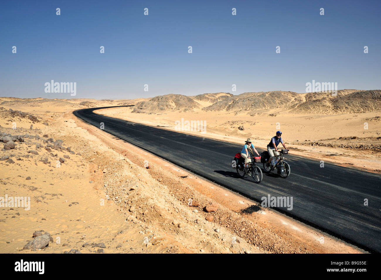 L'homme et de la femme de l'Ouest, complètement chargé sur des vélos de randonnée sur la route goudronnée en désert de Nubie au Soudan du nord, l'Afrique Banque D'Images