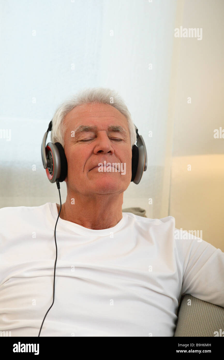 Salon canapé senior casque série portrait séance de relaxation personnes aînés retraités l'homme aux cheveux blanc entend-musique Banque D'Images