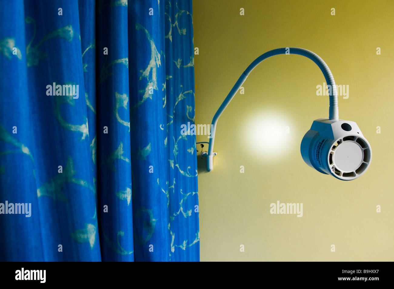 La lumière dans un cabinet médical qui brille sur un mur jaune, bleu rideau a été tiré autour d'un patient. Banque D'Images