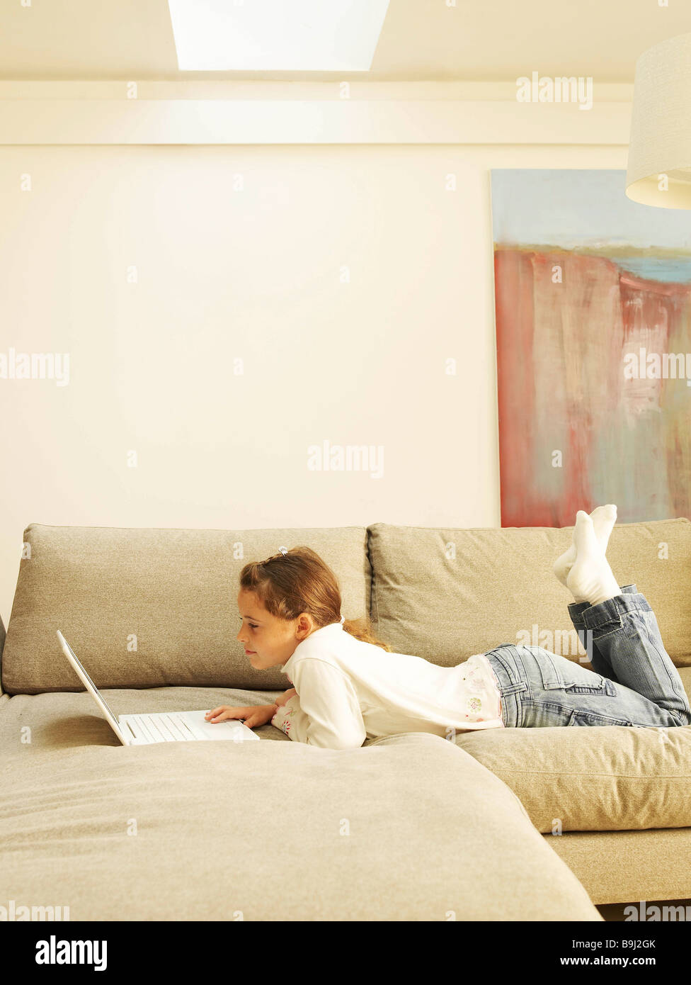 Girl lying on sofa using laptop Banque D'Images