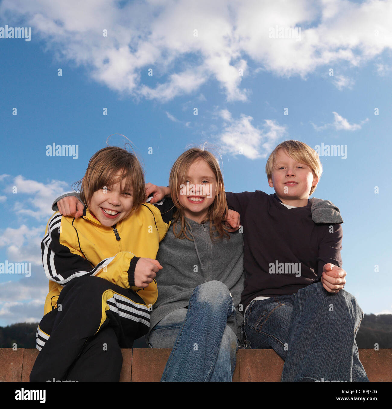 3 enfants assis sur un mur bas, smiling Banque D'Images