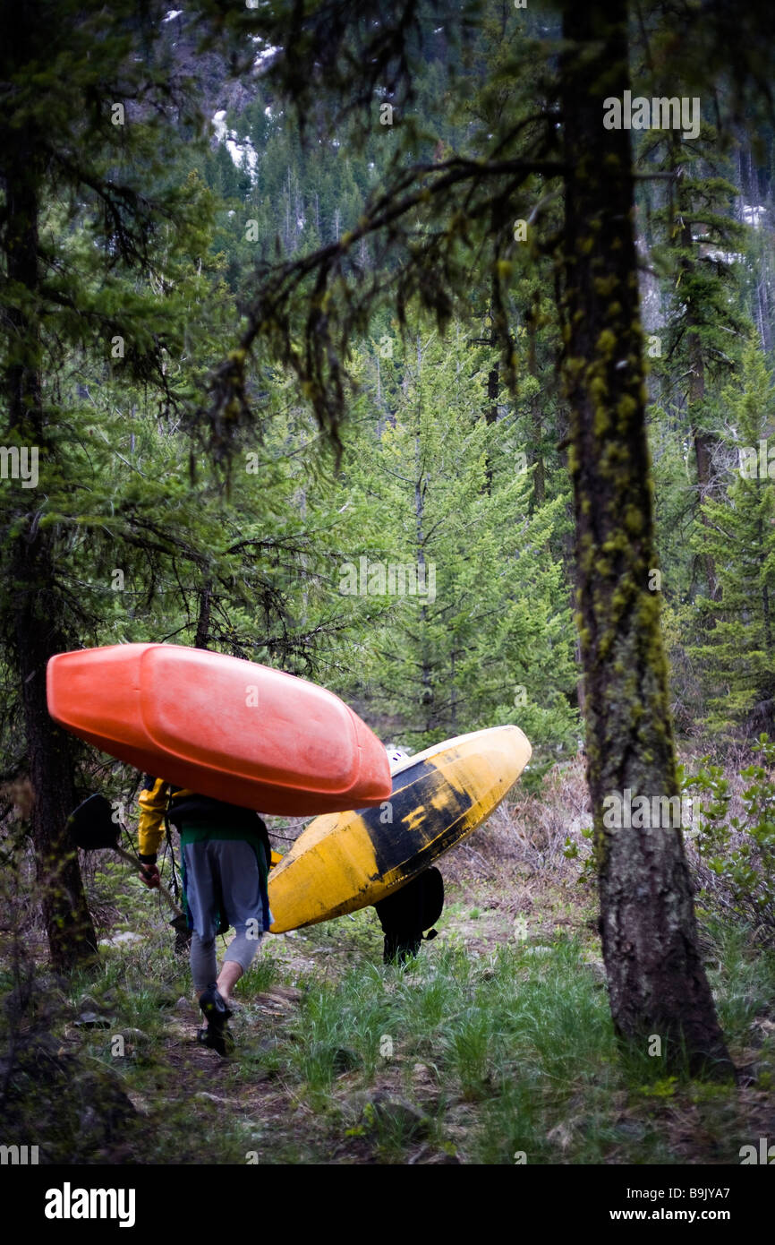 Deux kayakistes transporter leurs bateaux à travers une forêt sombre au Put-in. Banque D'Images