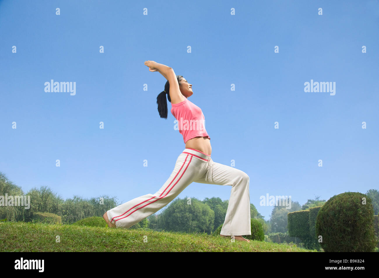 Woman practicing warrior 1 poser du yoga dans un parc Banque D'Images