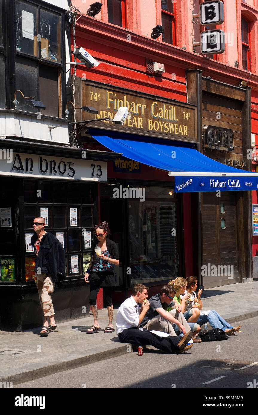 L'Irlande, dans le comté de Cork, Cork, les jeunes gens assis sur le trottoir Banque D'Images