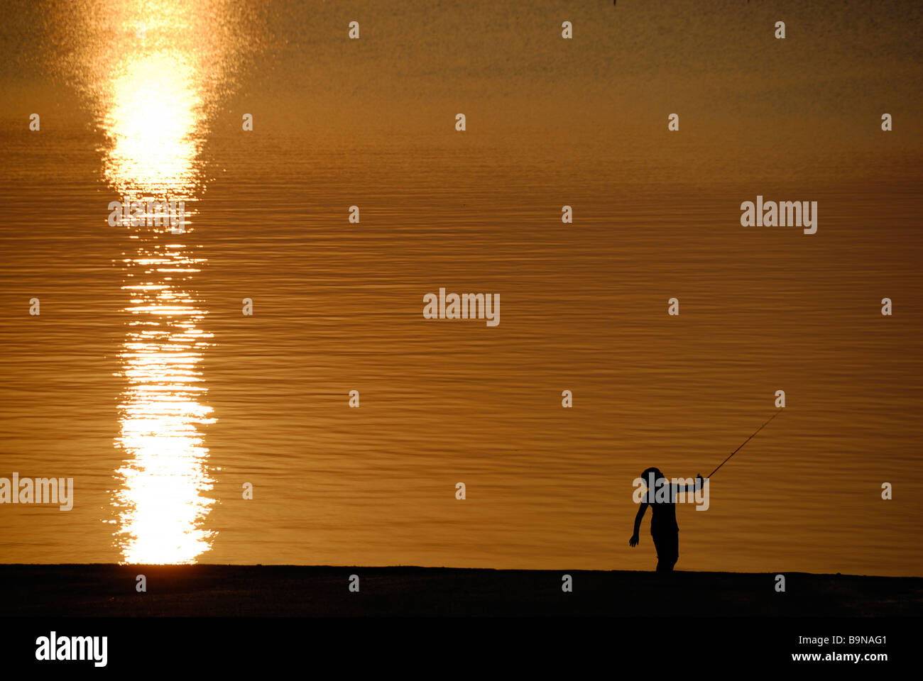 La silhouette d'un garçon appréciant les joies de la pêche au coucher du soleil Banque D'Images