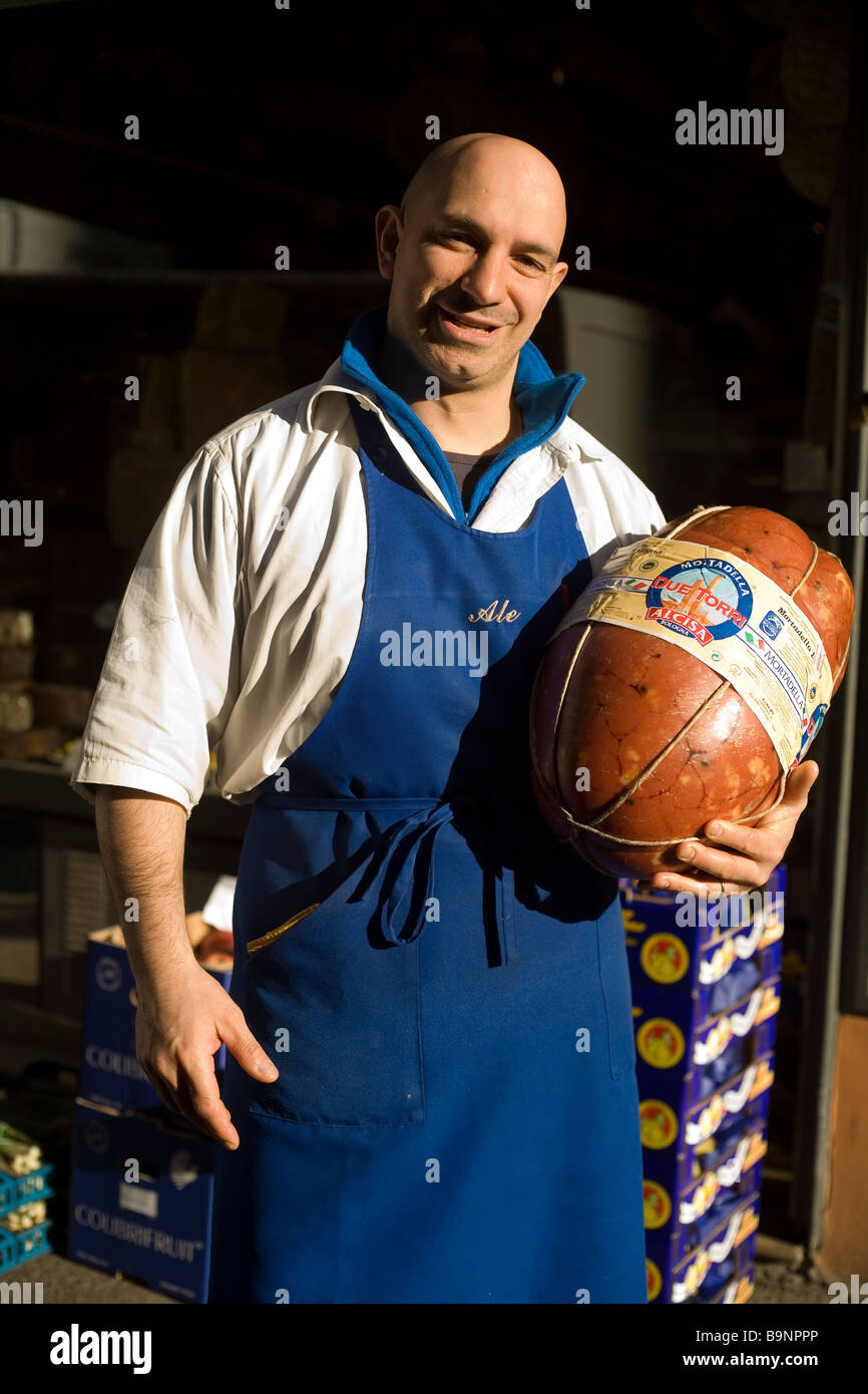Un boucher détient un grand jambon dans le seuil de sa boutique dans le Mercato di Mezzo Bologna Italie Banque D'Images
