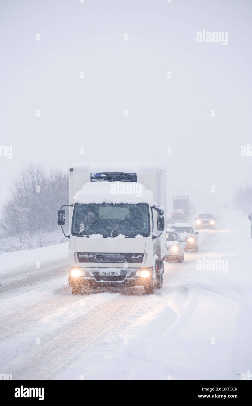 Camion DAF avec conducteur utilisant un téléphone portable et circulation après avoir roulé le long d'une route enneigée en hiver en Angleterre. Banque D'Images