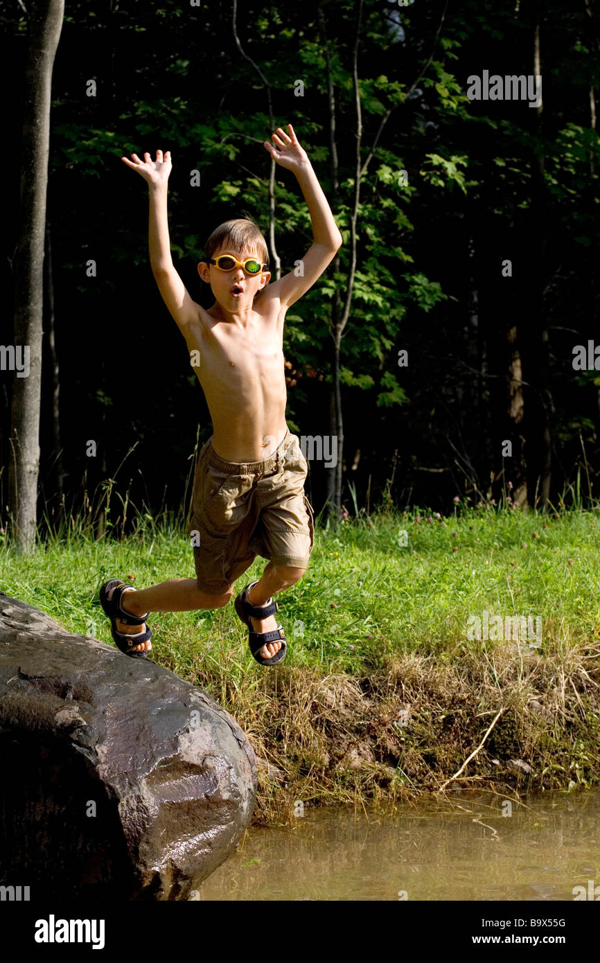 9 ans de sauter un rocher dans un étang Banque D'Images