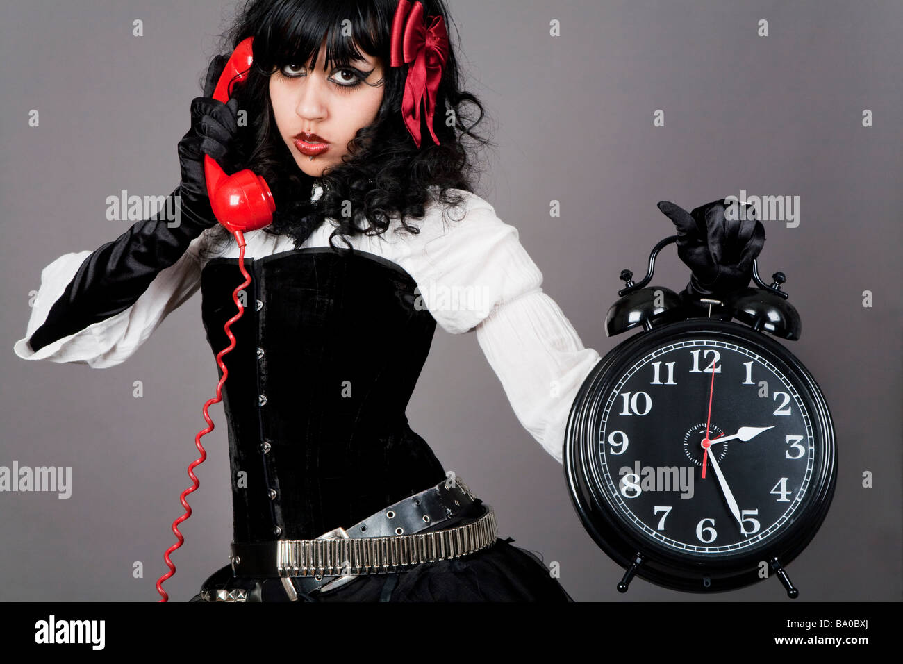 Jeune femme tenant un réveil et de parler sur un téléphone rétro rouge Banque D'Images