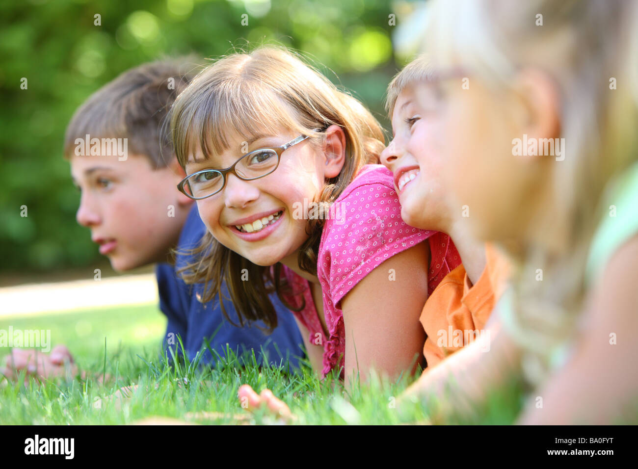 Groupe d'enfants laying in grass, une fille ressemble à l'appareil photo Banque D'Images