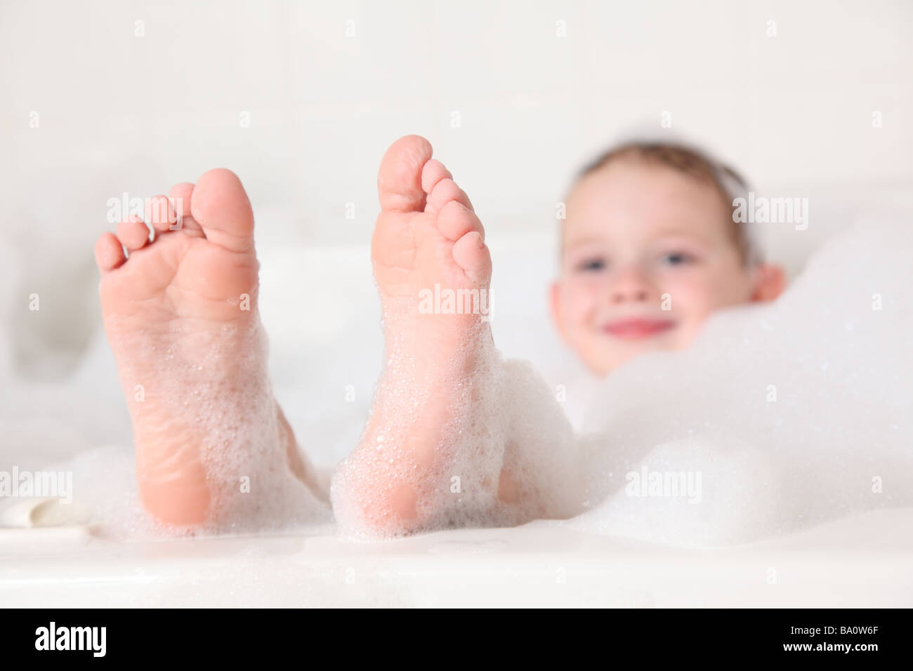 Jeune garçon avec pieds dépassant du bain de mousse Banque D'Images