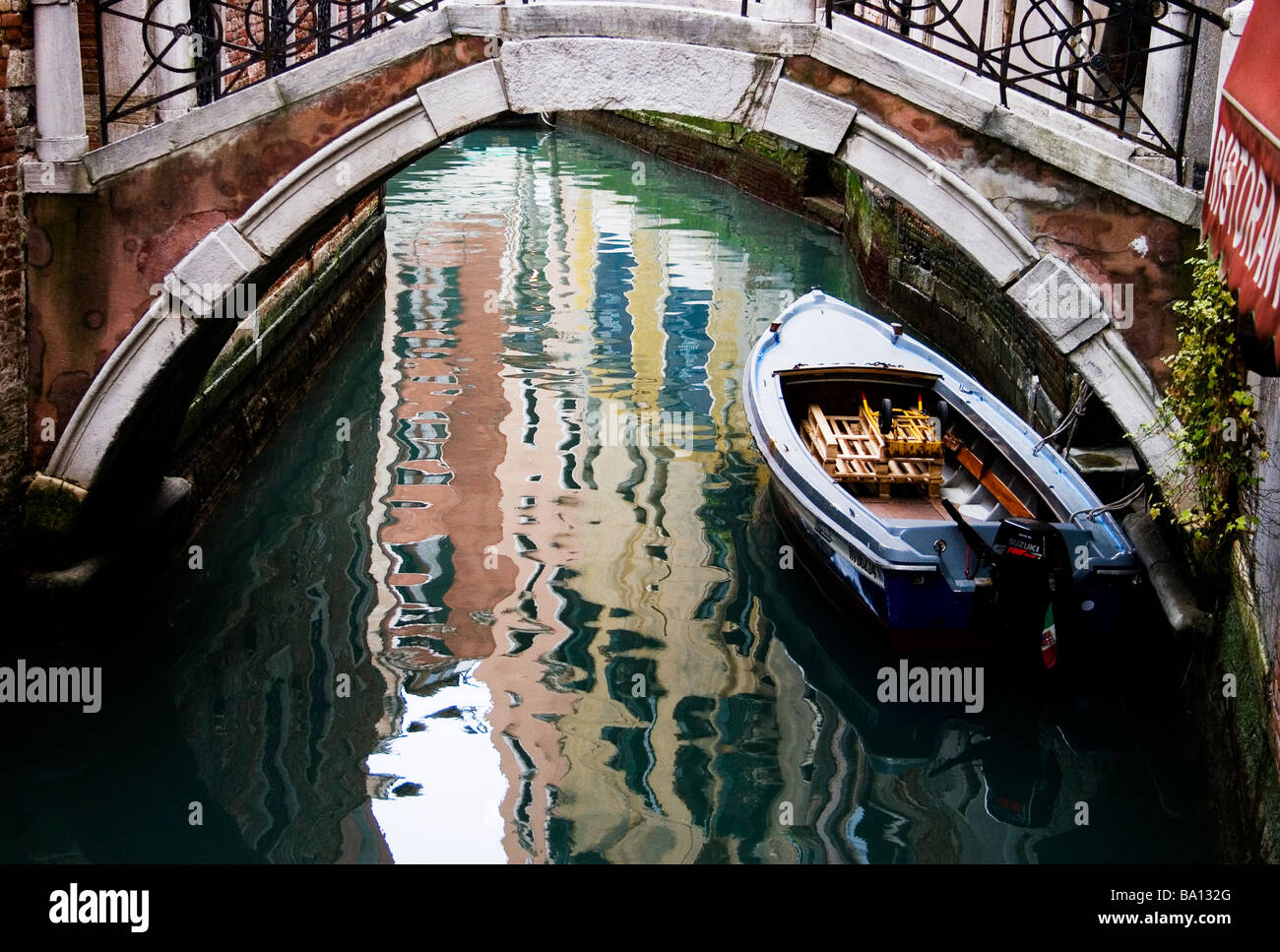 Bateau à moteur sous le vieux pont vénitien avec des bâtiments reflétés dans le canal d'eau à Venise, Italie Banque D'Images