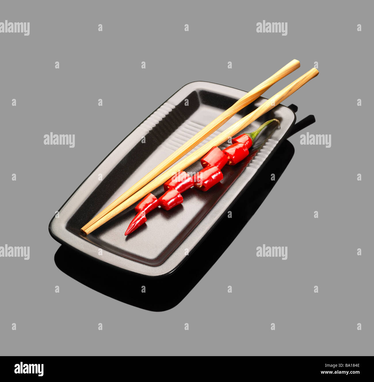 Piments rouges frais sur une plaque avec chopstikcs sur gray reflective surface Banque D'Images