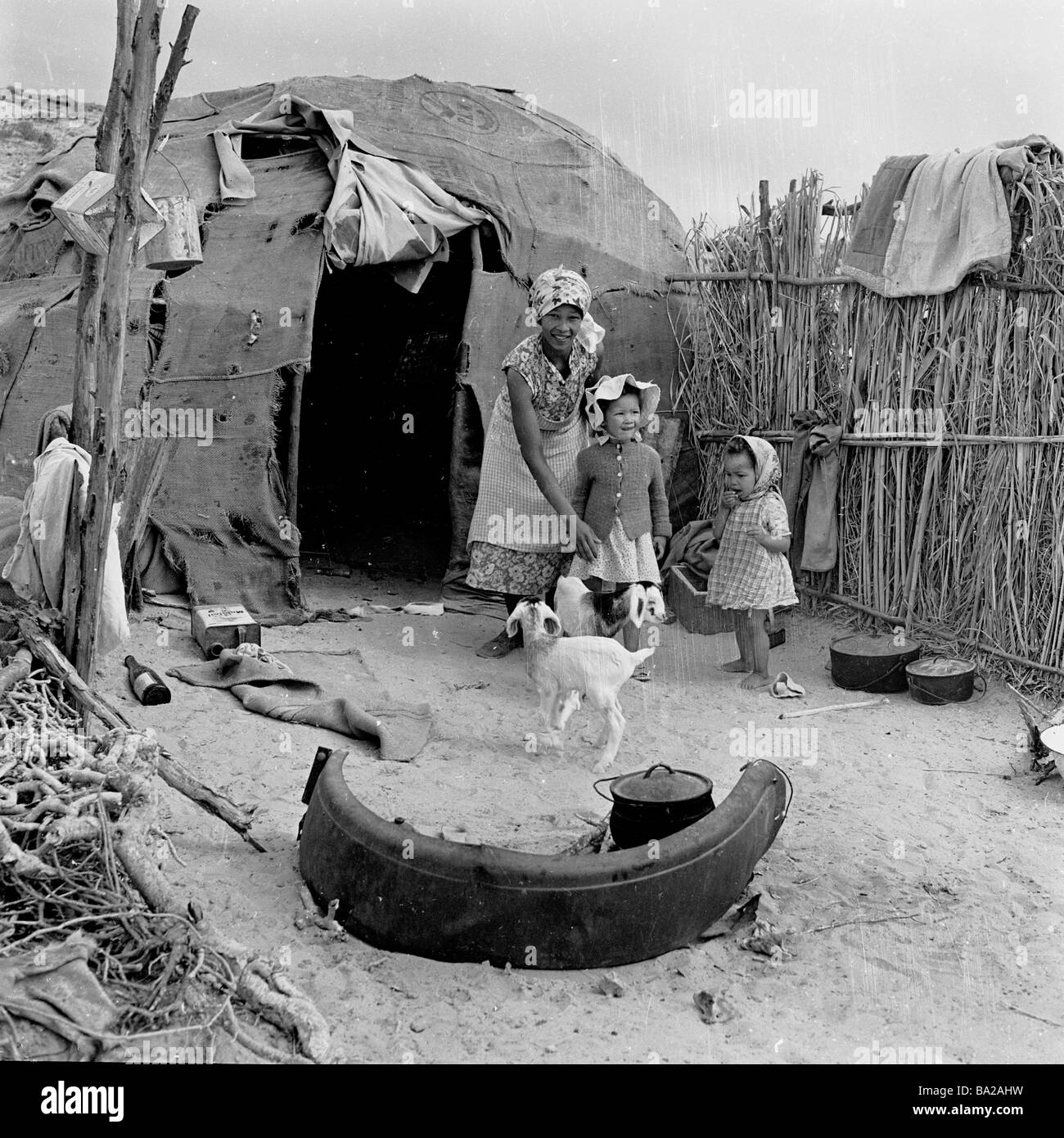 1950s, une mère avec ses deux enfants et un animal de compagnie à l'extérieur de leur maison, une tente de patchwork dans une colonie intérieure à Alexander Bay, Namaqualand, Afrique du Sud. Banque D'Images