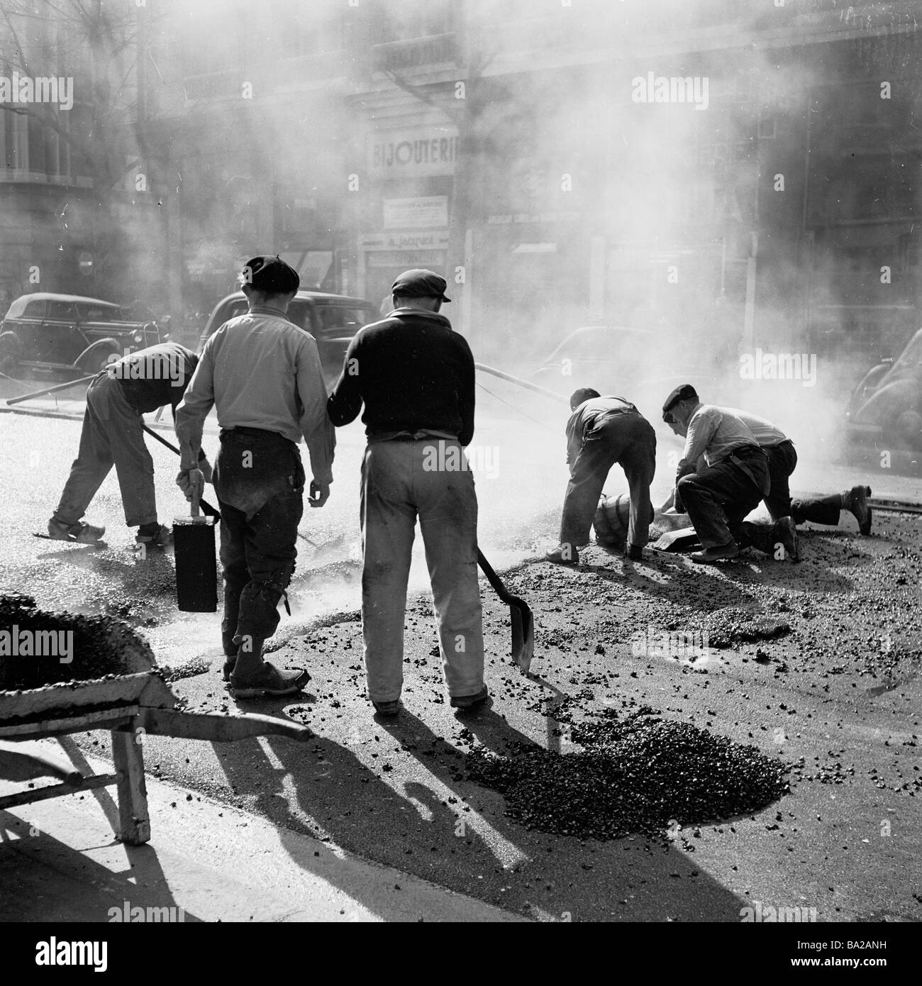 1950s,Paris, France, un groupe de travailleurs français réparant la surface de la route et posant du goudron chaud sur le célèbre boulevard Haussmann, une célèbre avenue parisienne Banque D'Images