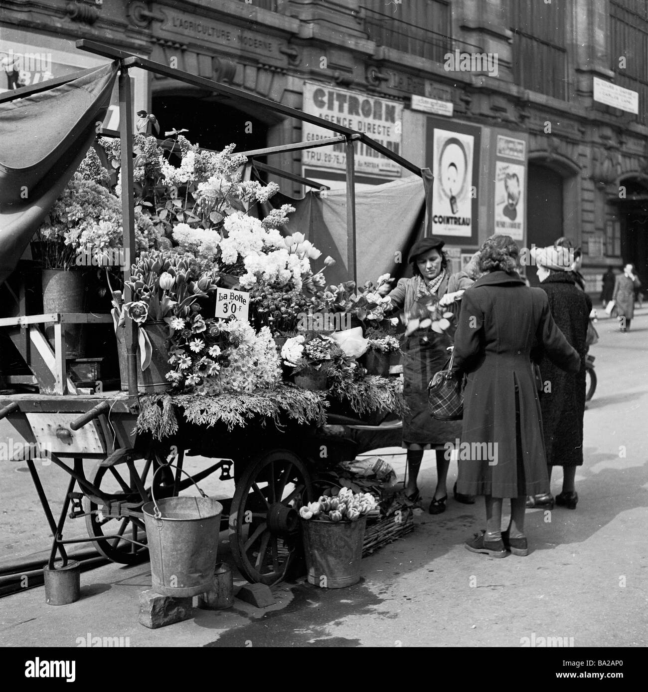 1950s, historique, de jour et une négociante féminine sert deux clientes à son stand de fleurs en plein air dans le Cadet, Opéra, Paris, France. Banque D'Images