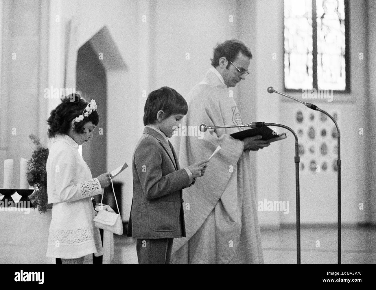 Années 70, photo en noir et blanc, la religion, le christianisme, Première Communion, fille et garçon avec un prêtre pendant la messe eucharistique, âgés de 8 à 12 ans, de 35 à 45 ans Banque D'Images