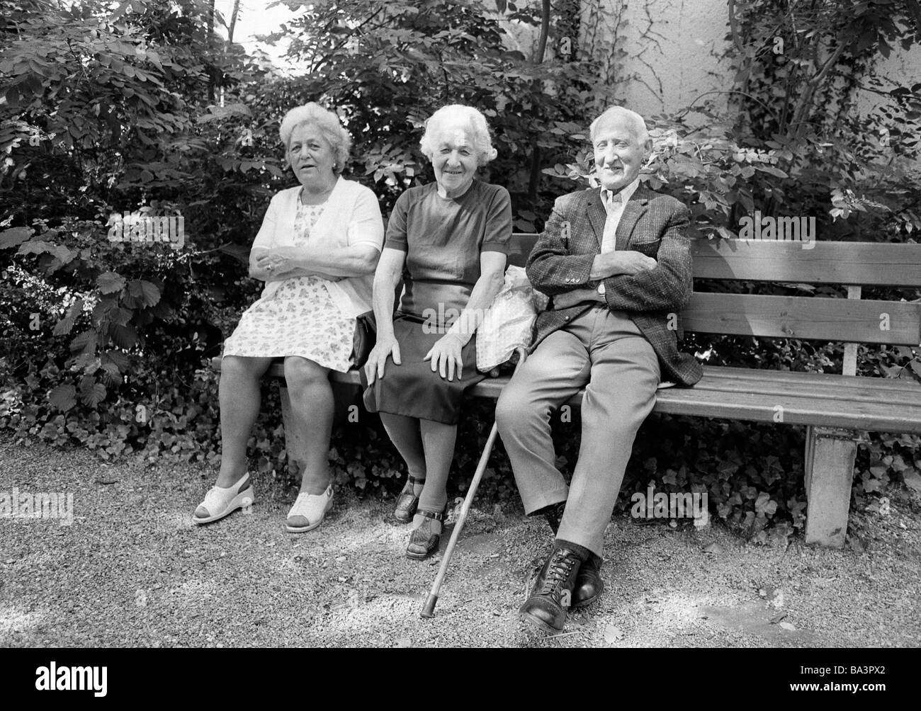 Années 1980, photo en noir et blanc, les gens, les personnes âgées, deux femmes âgées et un homme plus âgé assis sur un banc, robe, gilet, veste, pantalon, âgés de 70 à 80 ans Banque D'Images