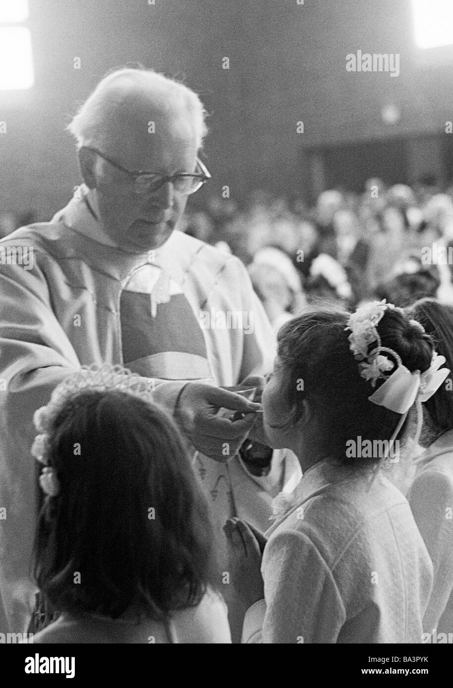 Années 70, photo en noir et blanc, la religion, le christianisme, Première Communion eucharistique, la messe, prêtre administre la Sainte Communion à une fille, âgés de 8 à 12 ans, de 55 à 65 ans, Babette Banque D'Images