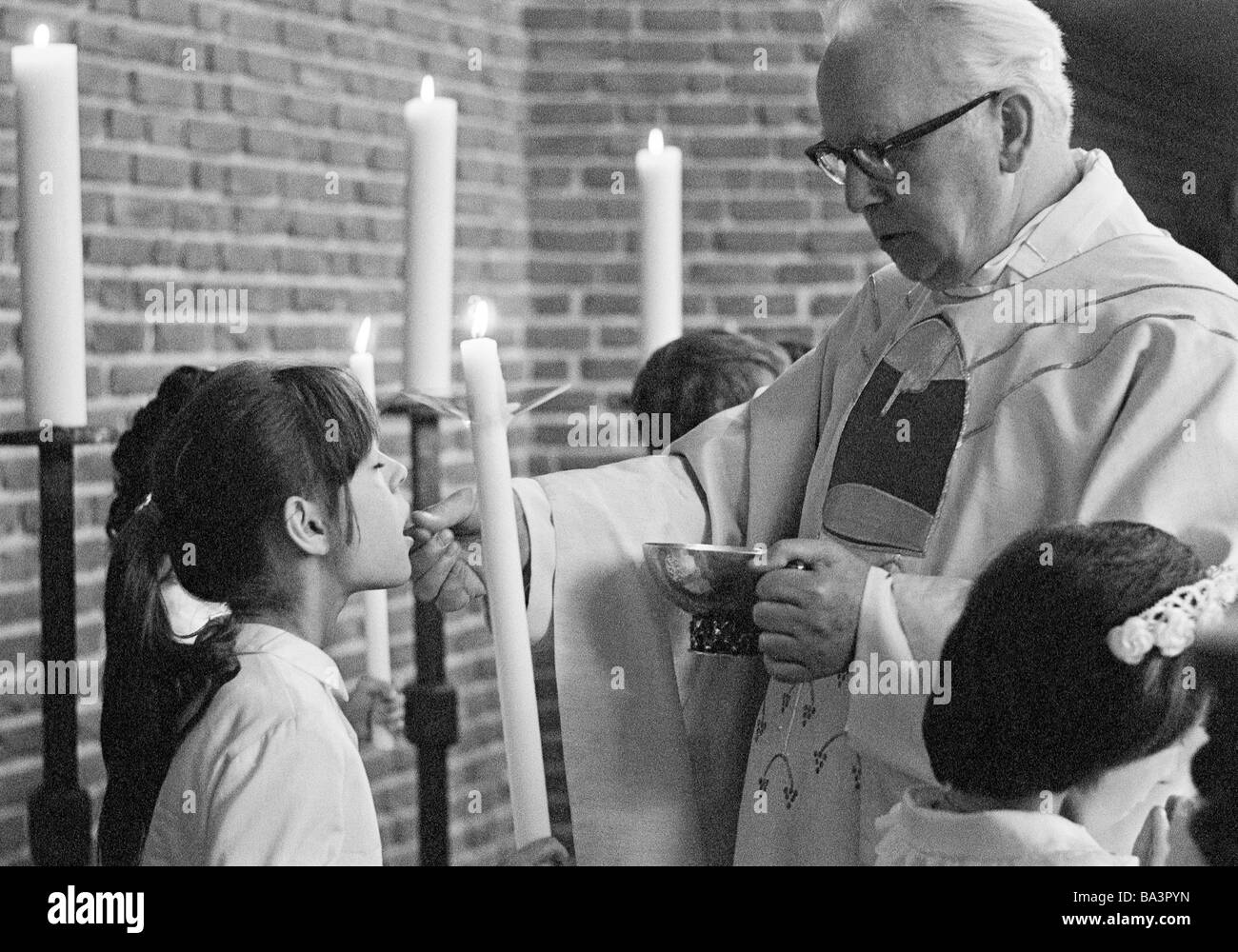 Années 70, photo en noir et blanc, la religion, le christianisme, Première Communion eucharistique, la messe, prêtre administre la Sainte Communion à une fille, âgés de 8 à 12 ans, de 55 à 65 ans Banque D'Images