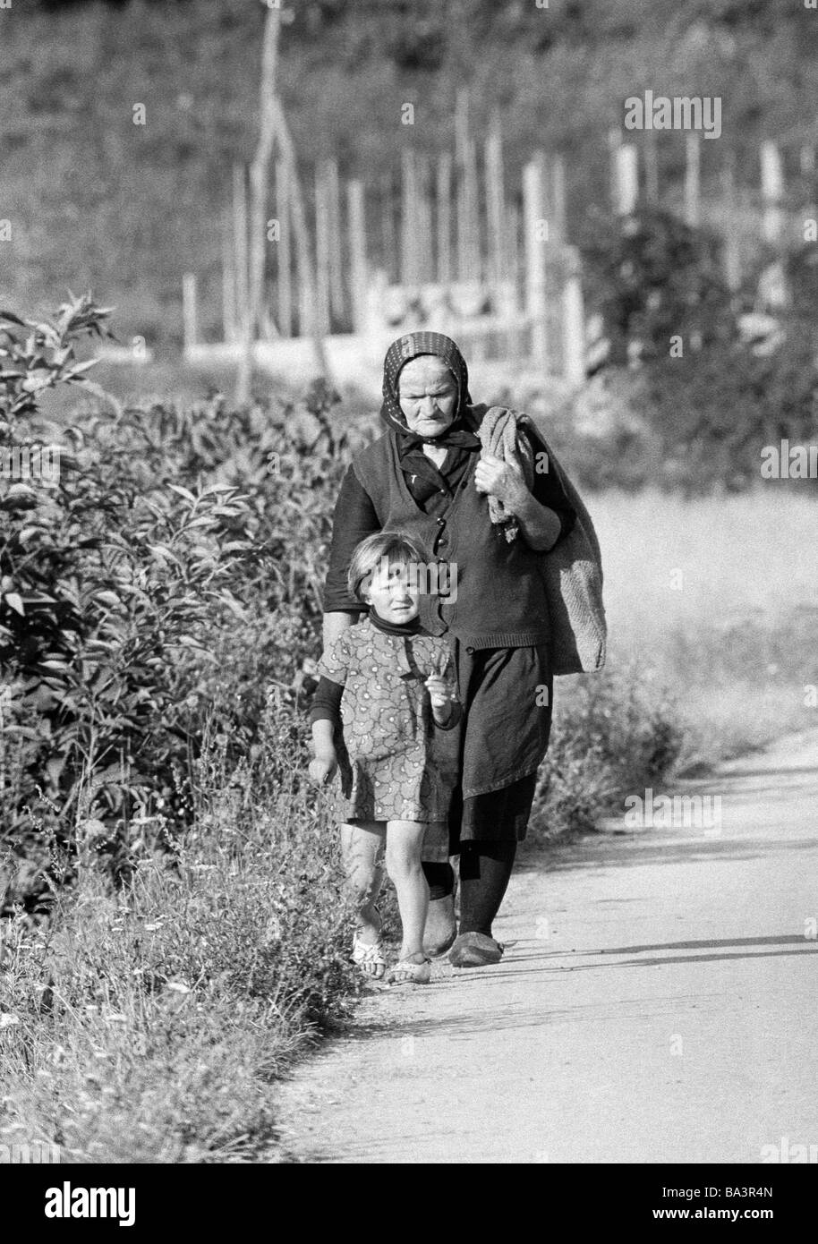 Années 70, photo en noir et blanc, les gens plus âgés, femme et son arrière-petite-fille marcher sur le raoadside d'une route de campagne, âgés de 70 à 80 ans, de 4 à 6 ans, en Croatie, à l'époque, la Yougoslavie Yougoslavie Banque D'Images