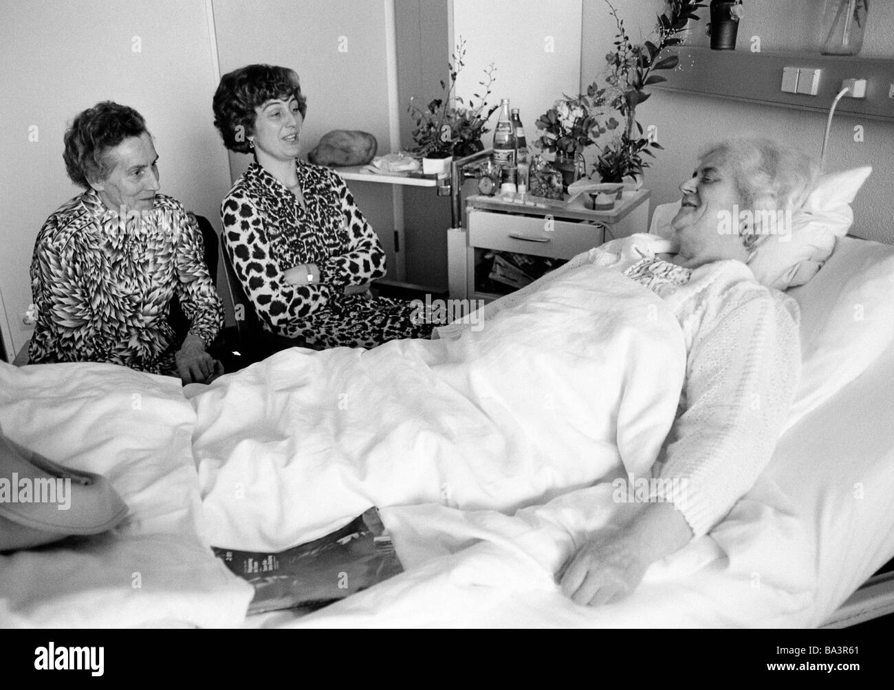 Années 1980, photo en noir et blanc, des gens, de la santé, femme plus âgée se trouve dans un lit d'un hôpital, deux femmes visitez son assis à côté du lit, âgés de 70 à 80 ans, de 50 à 60 ans, de 40 à 50 ans Banque D'Images