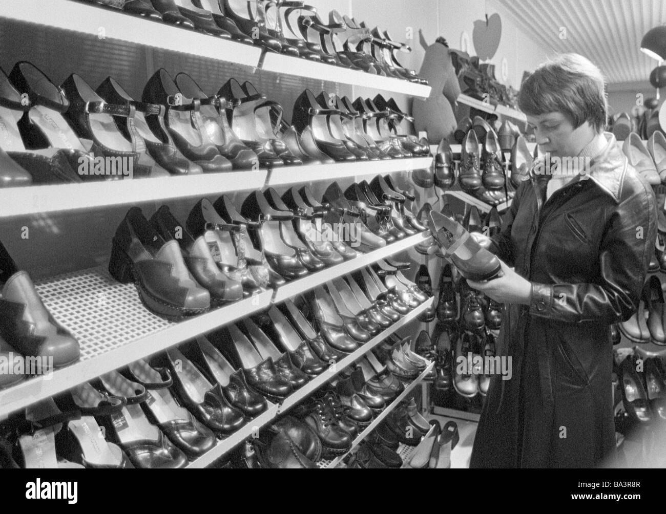 Années 70, photo en noir et blanc, de l'économie, le commerce de détail, jeune femme dans un magasin de chaussures, des étagères avec des chaussures, âgés de 20 à 25 ans, Monika Banque D'Images