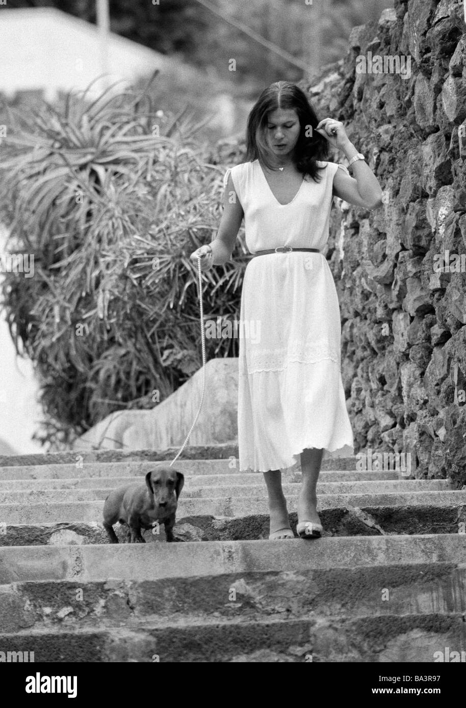 Années 1980, photo en noir et blanc, de l'homme et des animaux, les jeunes femme entre un teckel en laisse, âgés de 25 à 35 ans, chien domestique, Canis lupus familiaris, Espagne, Îles Canaries, Tenerife, Puerto de la Cruz Banque D'Images