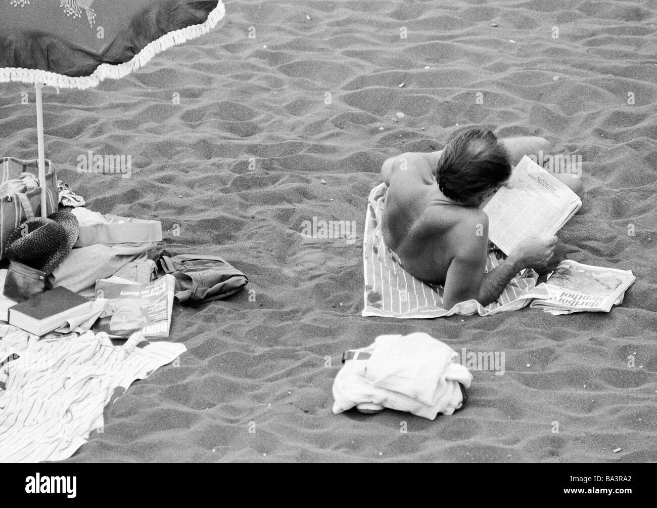Années 1980, photo en noir et blanc, Vacances, tourisme, l'homme se trouve sur la plage et lit un journal, l'Espagne, Îles Canaries, Tenerife, Puerto de la Cruz Banque D'Images