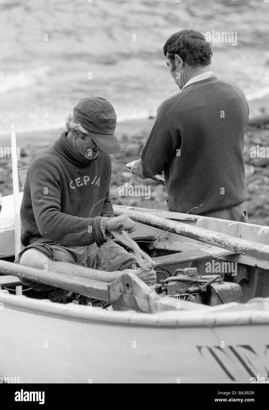 Années 1980, photo en noir et blanc, de l'économie, du port de pêche, pêcheur assis dans un bateau réparations un filet de pêche, de 60 à 70 ans, l'Espagne, Îles Canaries, Tenerife, Puerto de la Cruz Banque D'Images