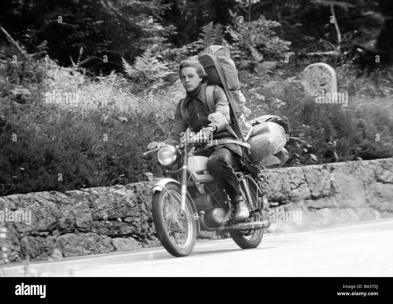 Années 70, photo en noir et blanc, le trafic routier, freetime, jeune homme va à une excursion avec sa moto, beaucoup de bagages sur le siège arrière, de 20 à 25 ans Banque D'Images