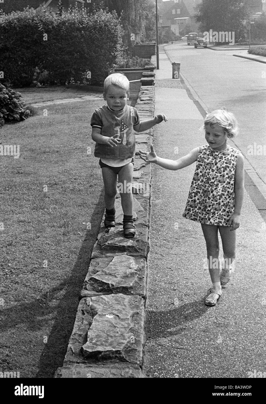 Années 70, photo en noir et blanc, les gens, les enfants, petit garçon marche sur un mur bas, petite fille marche à côté de lui et lui arrive, âgés de 3 à 4 ans, de 5 à 7 ans Banque D'Images