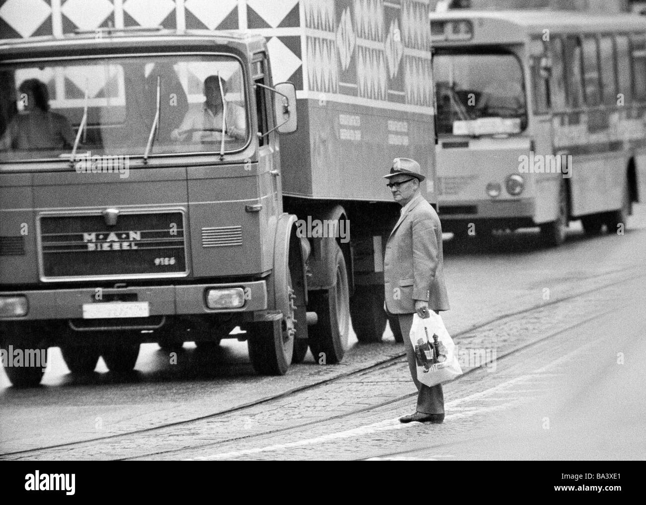 Années 70, photo en noir et blanc, personnage, homme plus âgé avec panier se dresse au milieu d'une circulation routière et tente de traverser la route, la circulation lourde, âgés de 65 à 75 ans Banque D'Images