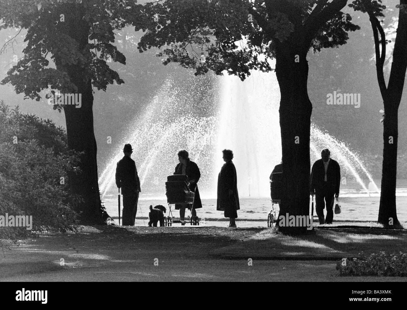 Années 70, photo en noir et blanc, les gens se promener dans un parc et se tenir en face d'une fontaine, rétroéclairage, silhouette, les personnes plus âgées, de 60 à 70 ans, landau, un chien, caniche, Stadtgarten, D-Bottrop, Ruhr, Rhénanie du Nord-Westphalie Banque D'Images