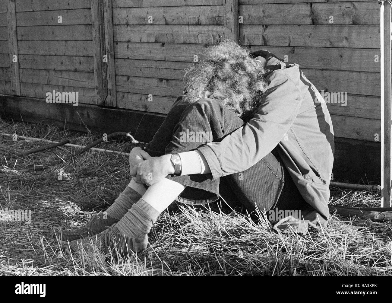 Années 70, photo en noir et blanc, les gens, les jeunes se recroquevilla en boule se trouve à proximité d'une clôture en bois, c'est triste, déprimé, âgés de 14 à 20 ans Banque D'Images