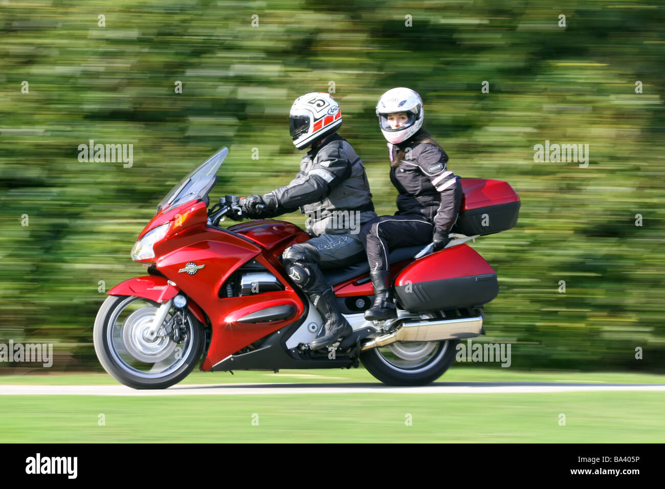 Moto rouge avec homme rider en noir cuir et leurs femmes les deux passagers portant des casques on rural road Banque D'Images