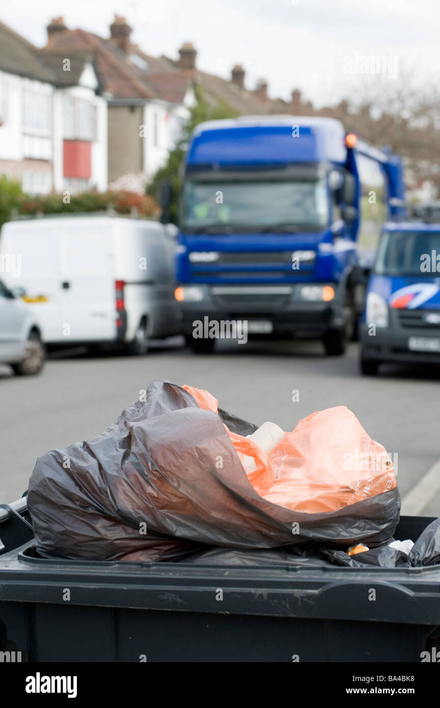 Poubelle noire pleine à ras bord en attente d'être recueillies sur une rue en Angleterre comme le camion poubelle à l'arrière-plan des approches Banque D'Images