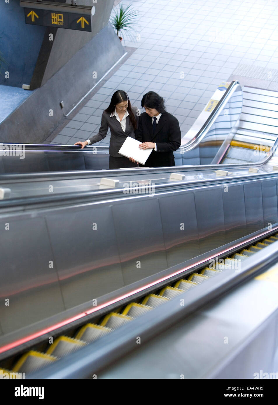 Businessman and businesswoman standing on escalator elevated view Banque D'Images