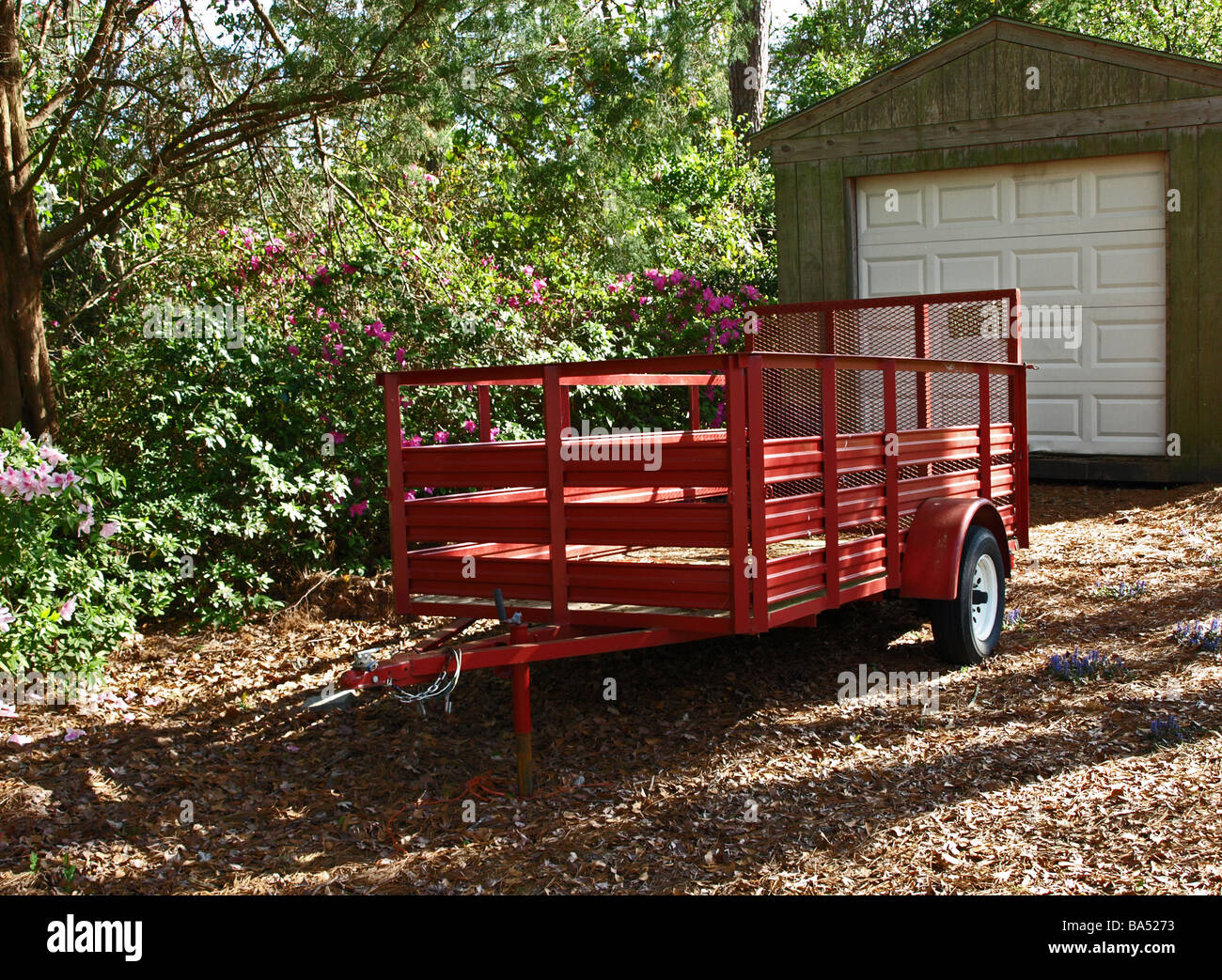 Remorque utilitaire rouge wagon utilisé pour transporter l'équipement outils fournitures aménagement paysager gazon garée avec l'attelage dans une cour ombragée par garage Banque D'Images