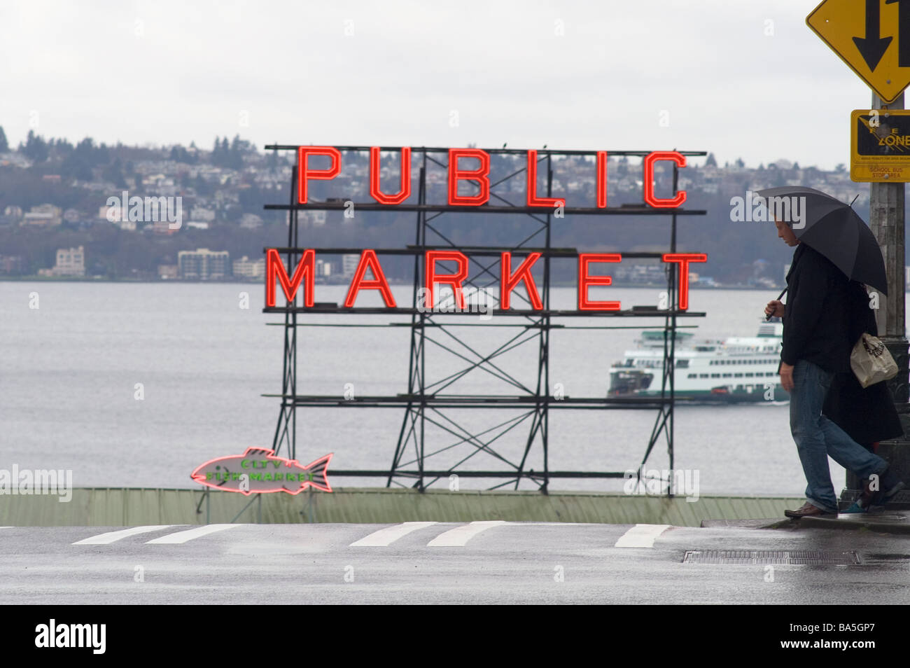 Les personnes qui traversent la rue à Seattle de pleuvoir la Première Avenue avec les agriculteurs de Pike Place Market signe et Elliot Bay Banque D'Images