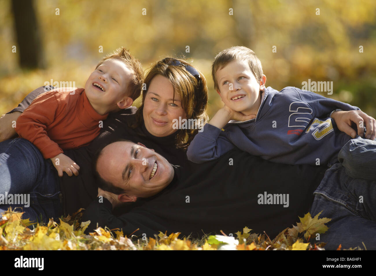 La famille se trouve automne feuillage gaiement rire regard caméra adultes parents les enfants garçons fils hors de feuillage de l'automne feuilles d'automne Banque D'Images
