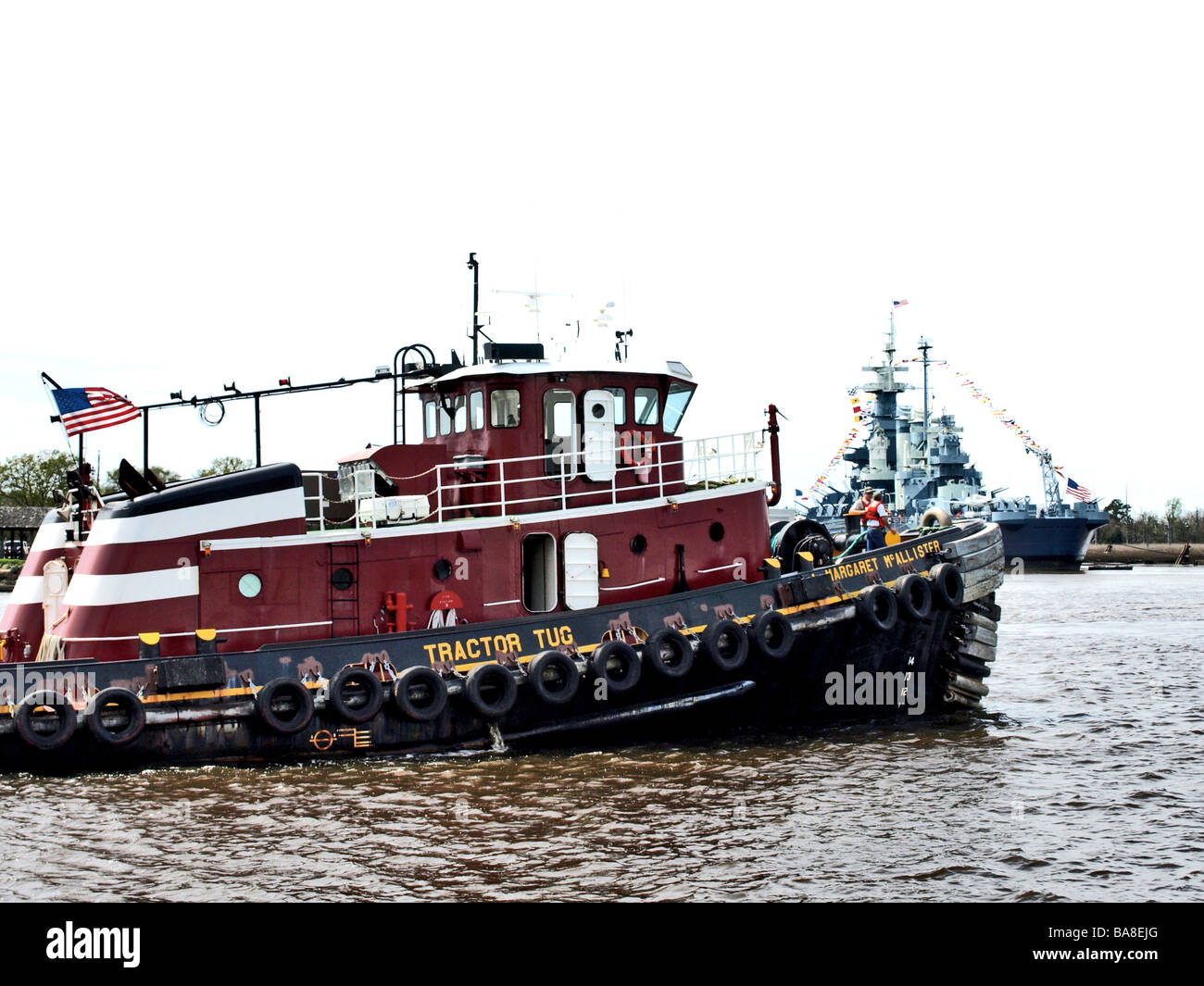 Tracteur tug boat sur la rivière Cape Fear, rouge avec des pneus et l'USS North Carolina en arrière-plan Banque D'Images