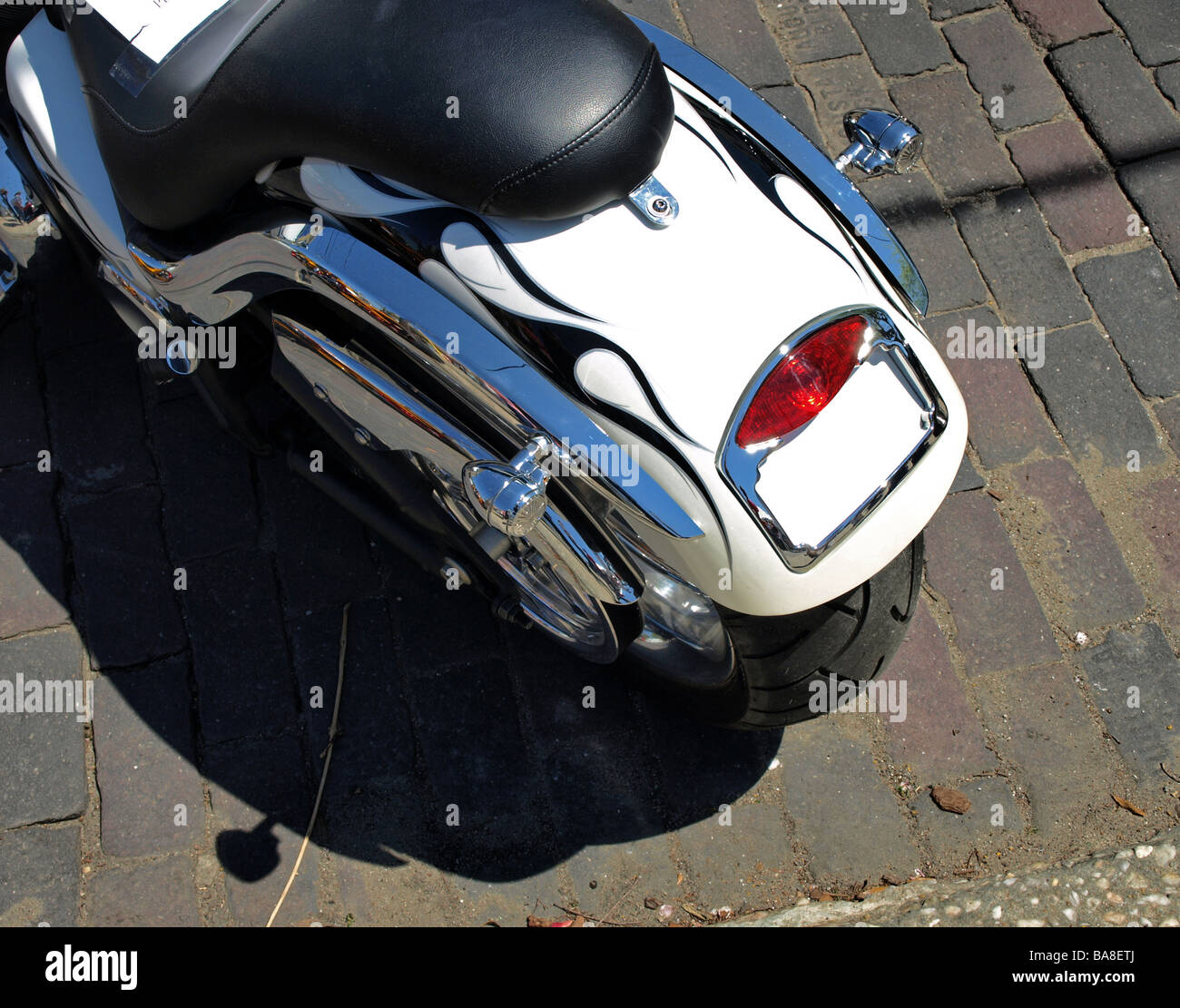 Roue arrière moto et siège avec flammes noires sur blanc et chrome tous les tuyaux sur la brique, de la rue et l'ombre de la plaque vide Banque D'Images