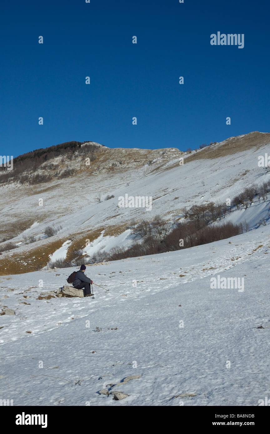 L'alpiniste est assis sur un rocher, le repos sous la montagne couverte de neige pendant la journée ensoleillée Banque D'Images