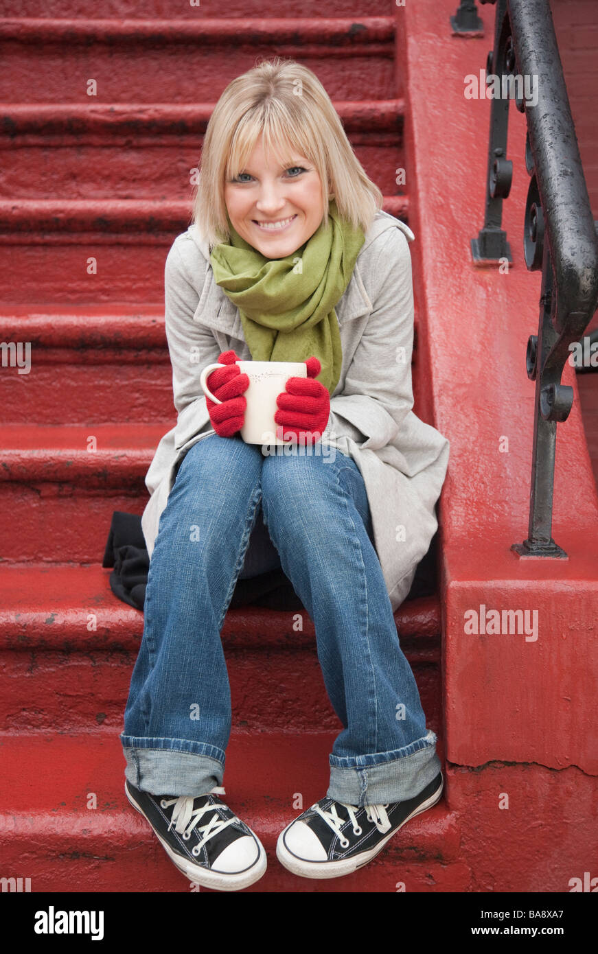 Femme buvant du chocolat chaud à l'avant stoop Banque D'Images