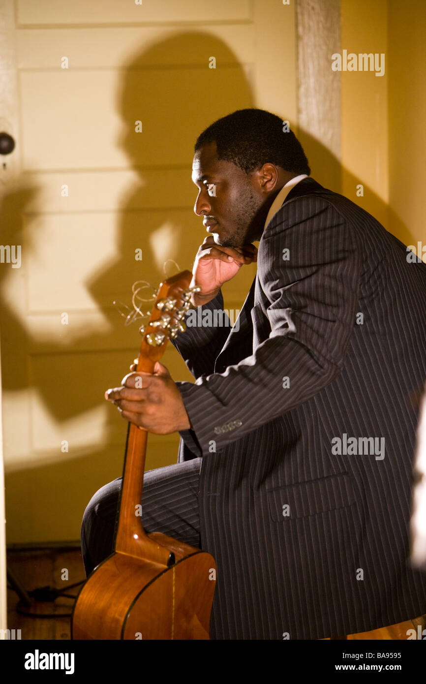 Musicien afro-américain siégeant en chambre avec guitare, side view Banque D'Images