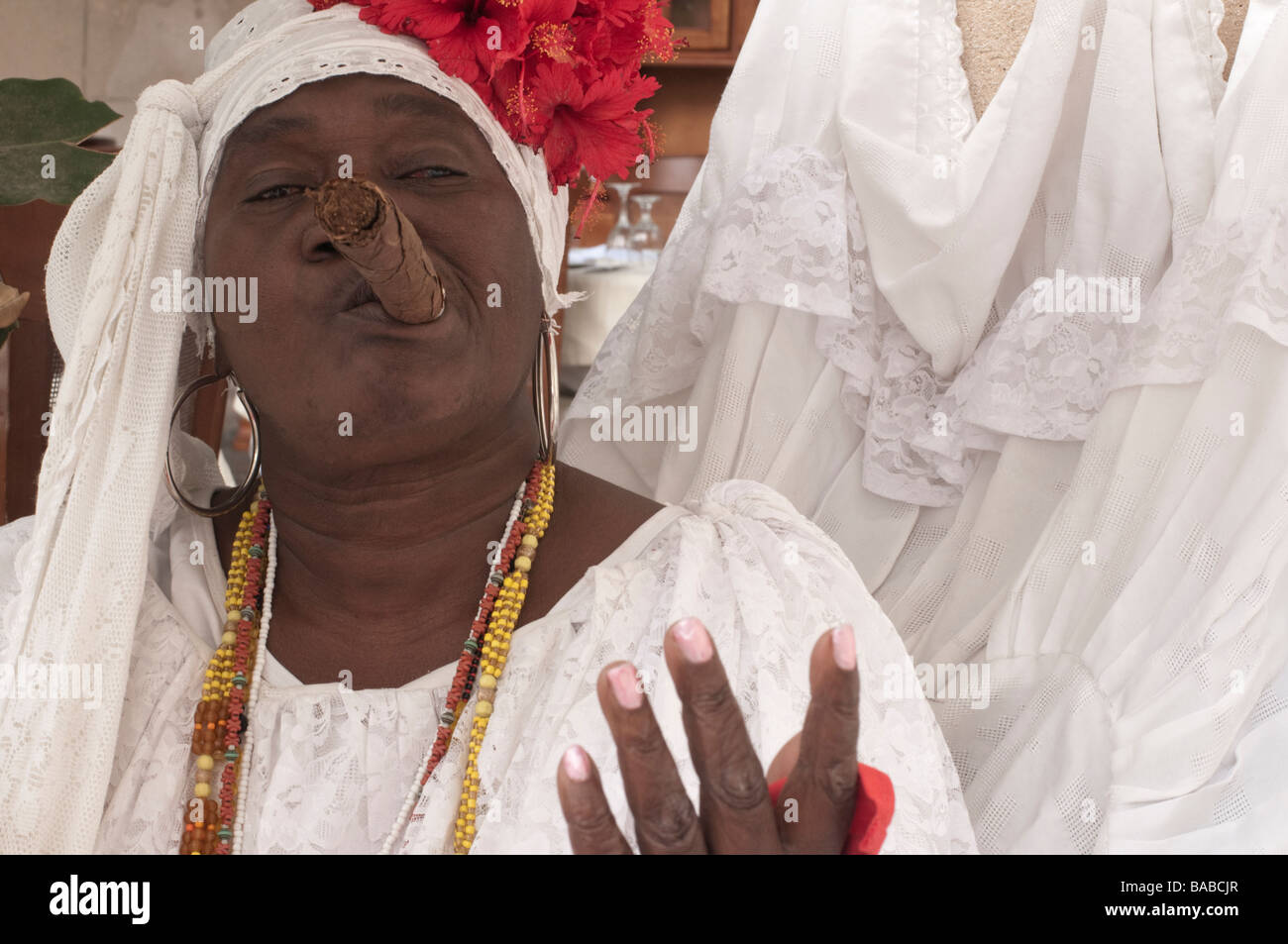 Femme fumant un gros cigare à La Havane Vieja avec une coiffe blanche et de fleurs. Banque D'Images