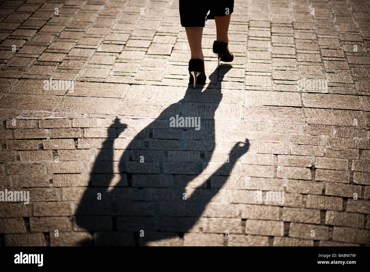 Vue arrière des jambes pieds et l'ombre d'une femme portant des talons hauts marcher seule le long d'un trottoir dans une ville Banque D'Images
