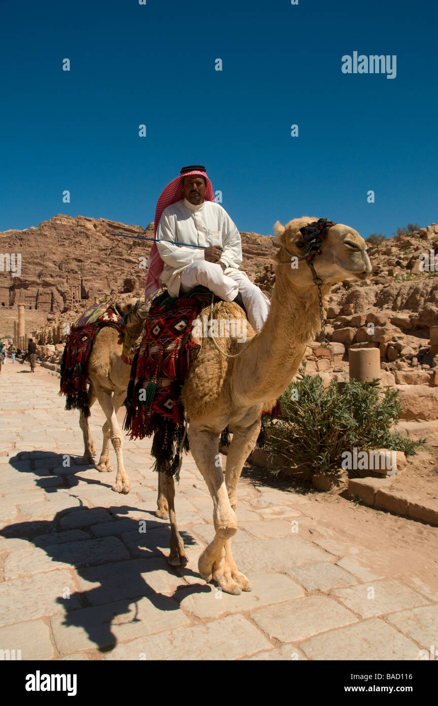 Un homme portant un keffieh à carreaux blancs et rouge monté sur un chameau dans l'ancienne ville nabatéenne de Pétra en Jordanie Banque D'Images